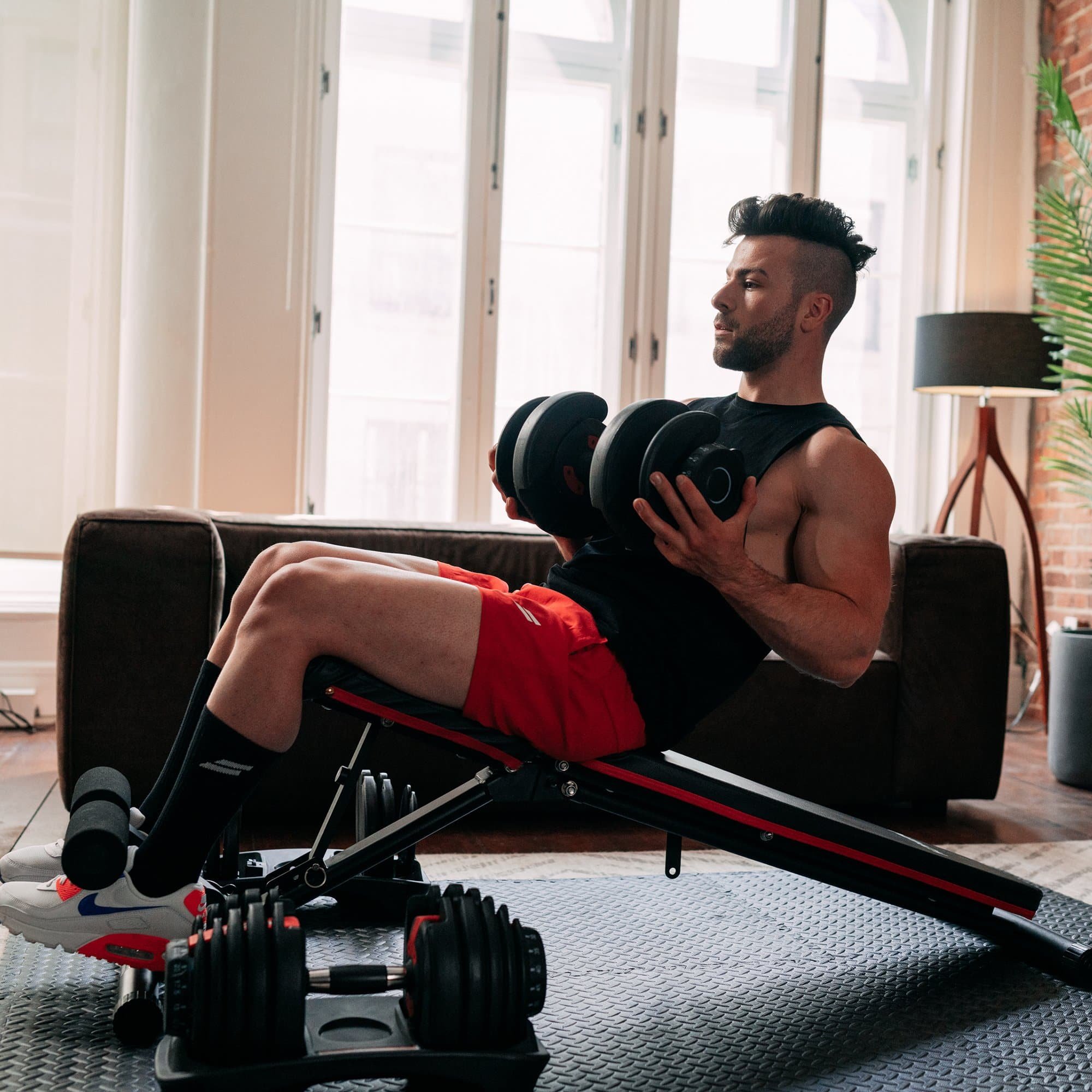 Man exercising with dumbbells on an incline bench in a living room.